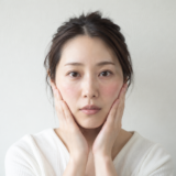 赤みのある頬に両手を添えている女性